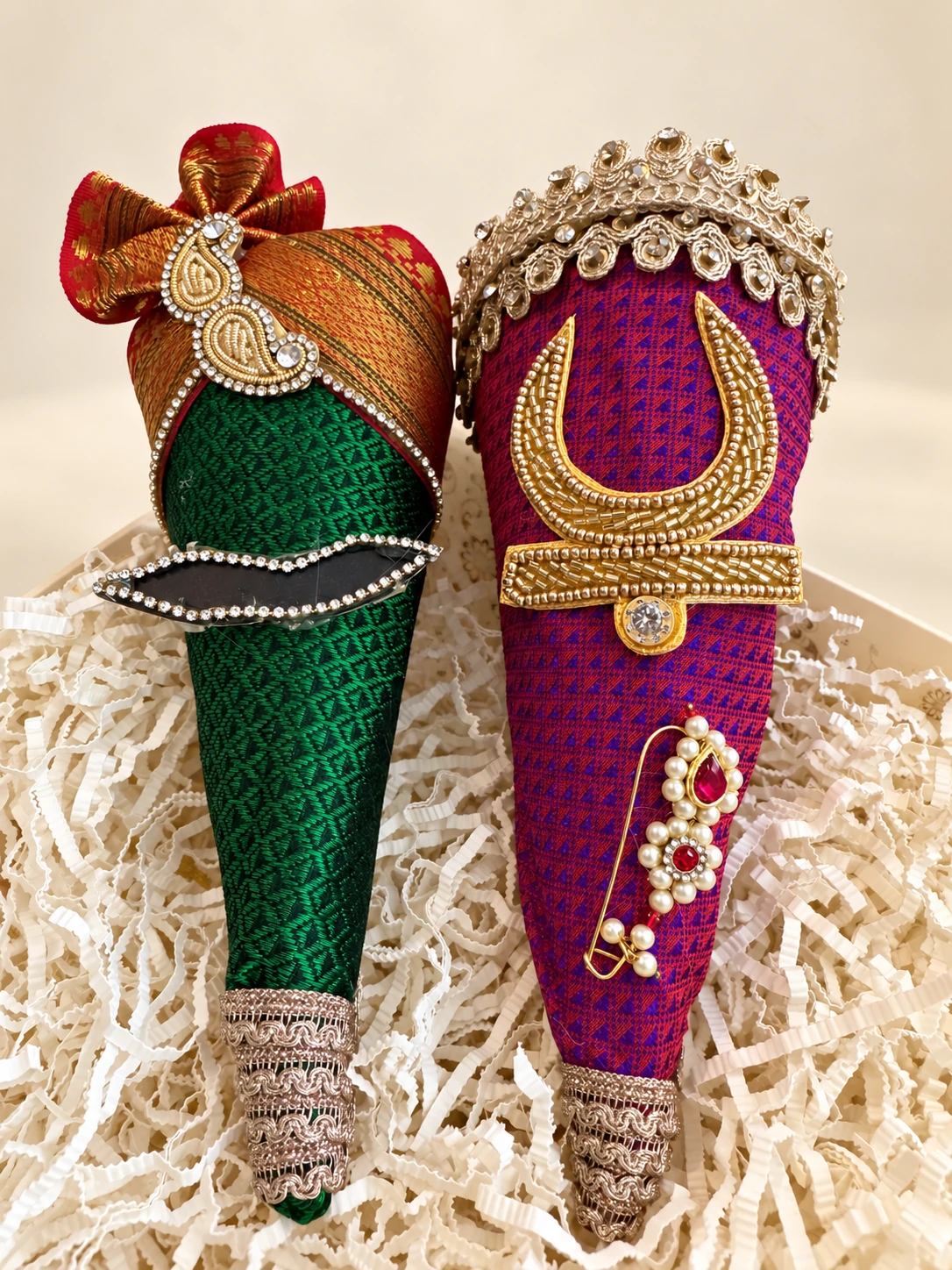 A pair of coconuts dressed as bride and groom, one with a turban and one with a nose ring, set in paper shred
