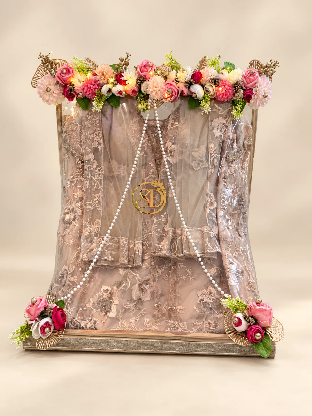 Framed trousseau display with a lace outfit, pearl strings and floral garland